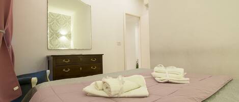 A neatly made bed with pink bedding, a wooden dresser with drawers, and a mirror on the wall.