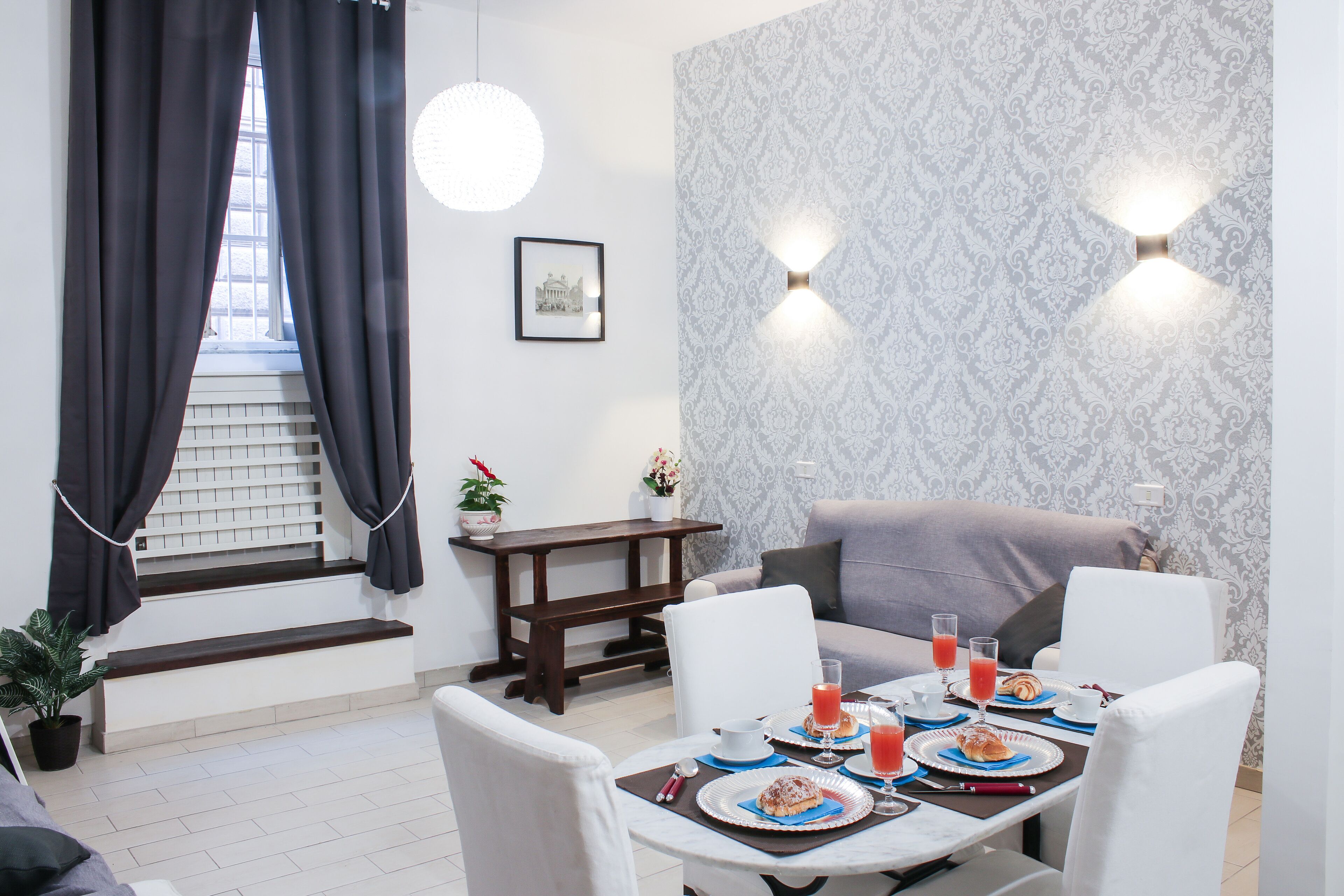 Uma sala de jantar com uma mesa posta para o café da manhã, um sofá, uma escada e um papel de parede estampado.