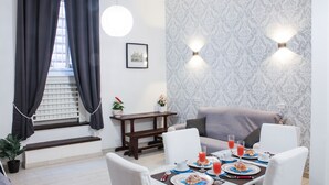 A dining area with a table set for breakfast, a sofa, a staircase, and a patterned wall.