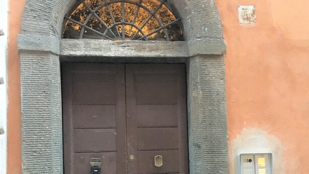 A brown double door with a metal grille above it, set within a stone archway.
