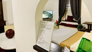A hotel room with a bed, a desk, a television, a vase with flowers, and a menu on the wall.