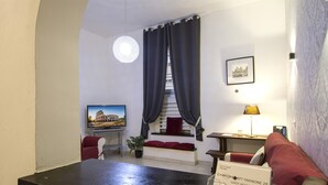 A hotel lobby with a reception desk, a seating area with red cushions, a staircase, and a framed picture on the wall.
