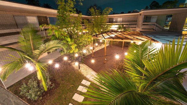 A courtyard with a wooden deck, palm trees, and string lights. - Stay Avenida Westshore (Tampa)