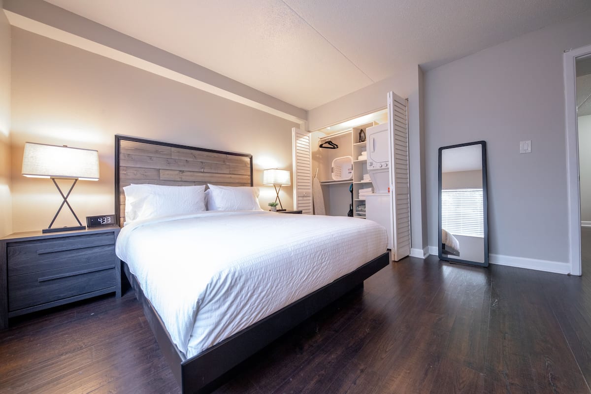 A neatly arranged bedroom with a large bed, bedside tables, a wardrobe, and a mirror.