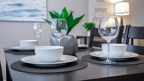 A dining table set with white bowls and wine glasses, a potted plant, and a lamp. - Stay Avenida Westshore (Tampa)