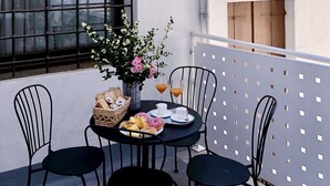 Una terraza en la azotea con una mesa preparada para dos personas, que incluye una cesta de pasteles, un jarrón de flores y dos vasos de zumo de naranja.