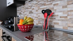 Una encimera de cocina con un bol estampado de lunares que contiene plátanos y naranjas, una tetera y un vaso con utensilios.