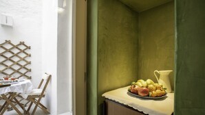 Eine kleine Küchenzeile mit Tisch und Stühlen, eine Obstschale auf der Arbeitsplatte und eine grüne Wand.