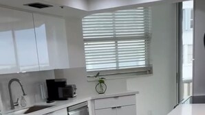 A modern kitchen with white cabinetry, a built-in dishwasher, a coffee maker, and a window with blinds. - Beautifully modern just renovated steps away from the Beach. (Miami Beach)