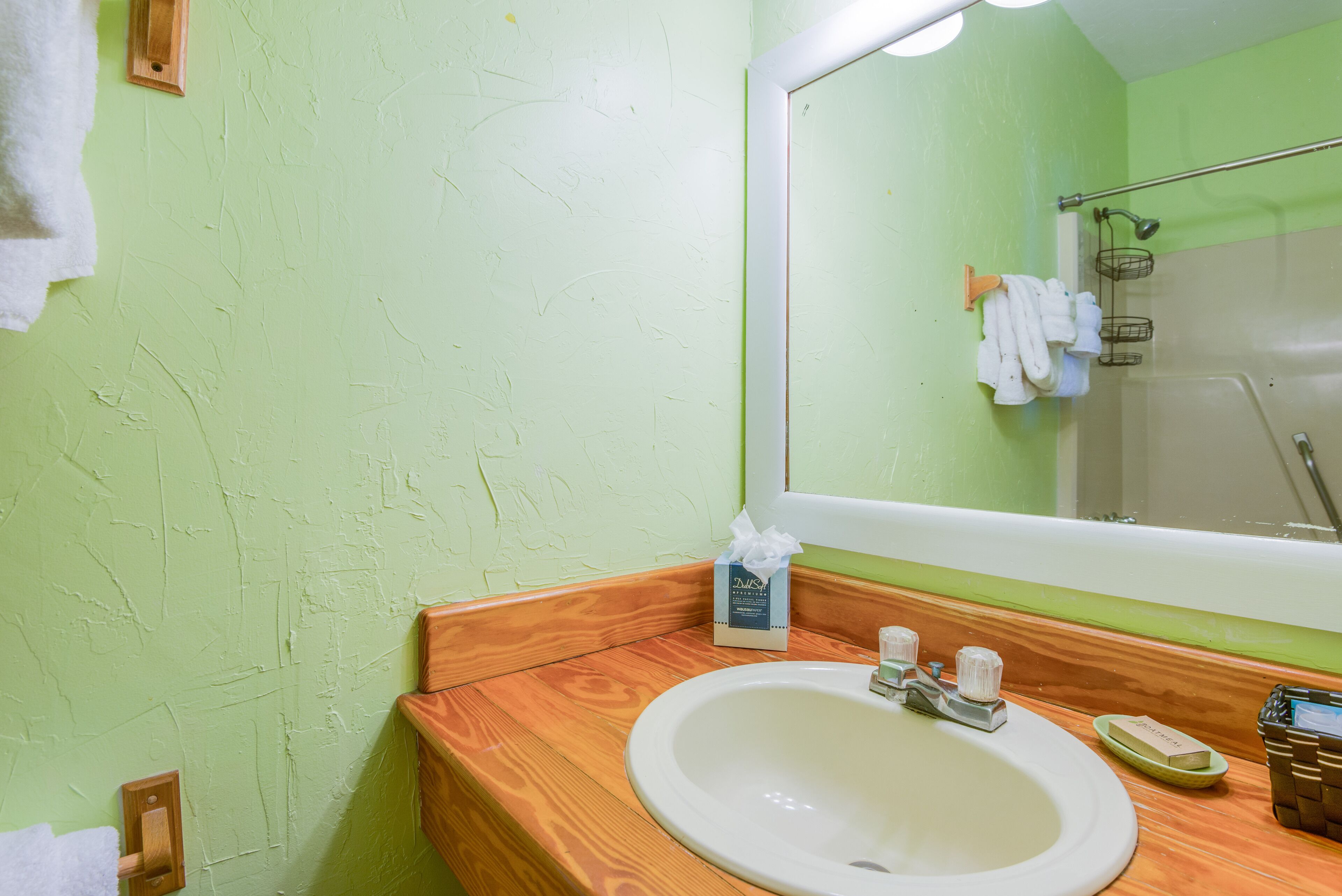 Une salle de bain avec un meuble-lavabo en bois, un lavabo blanc, un miroir et un mur vert.