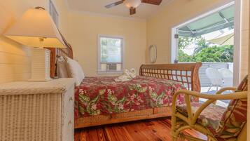 A bedroom with a bed, a wicker chair, a ceiling fan, and a window.