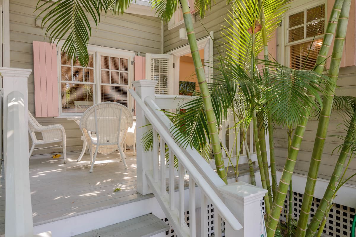 A covered porch with white wicker furniture, a staircase with white railings, and tall bamboo plants.
