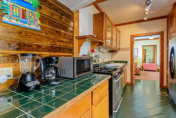A kitchen with wooden cabinets, a green-tiled countertop, a blender, a coffee maker, and a microwave.
