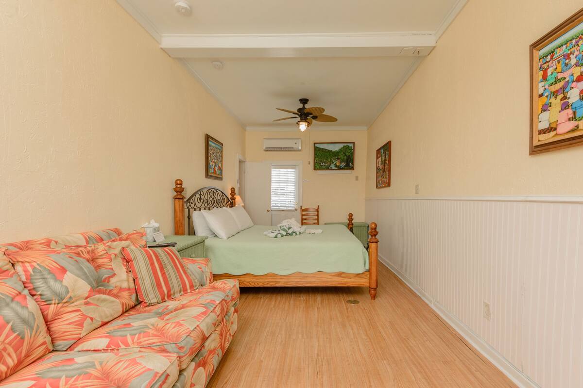 A bedroom with a bed, a floral-patterned sofa, a ceiling fan, and a window with blinds.