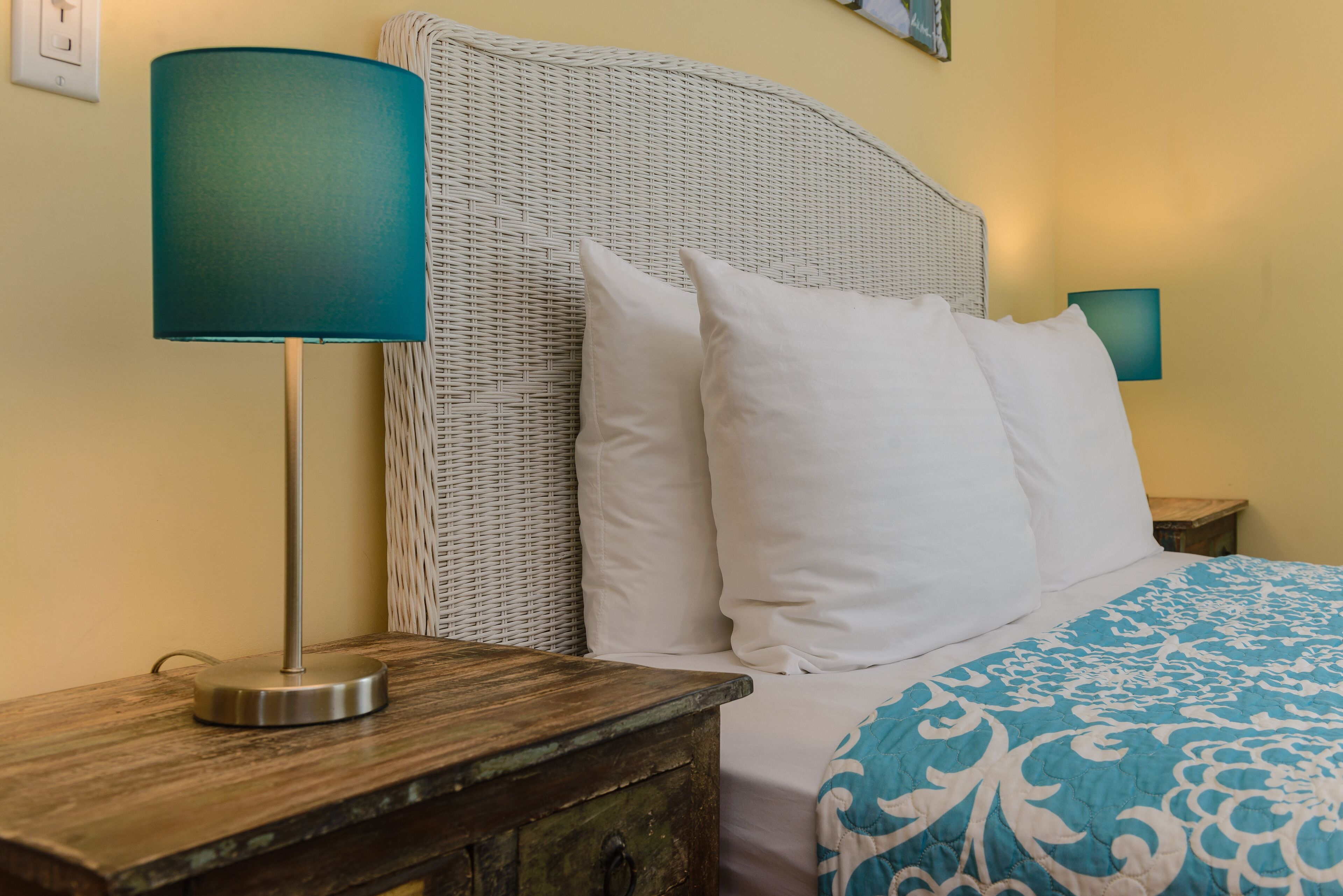 A bed with white pillows, a teal lamp, and a blue patterned bedspread.