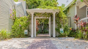 A covered entrance with a brick pathway leading to a gated area, surrounded by lush greenery and plants. - Key West Villas (Key West)