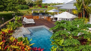 Une piscine avec une terrasse en bois, des chaises longues et un espace barbecue.