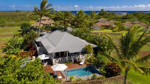 Une grande maison avec une piscine, entourée d’une végétation luxuriante et de palmiers, offrant une vue sur la côte.