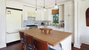 Une cuisine avec des meubles blancs, un îlot central en bois et un coin repas doté de chaises en osier.