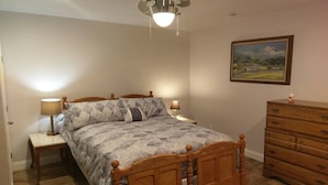 A bedroom with a wooden bed, two bedside tables with lamps, a dresser, and a landscape painting on the wall.