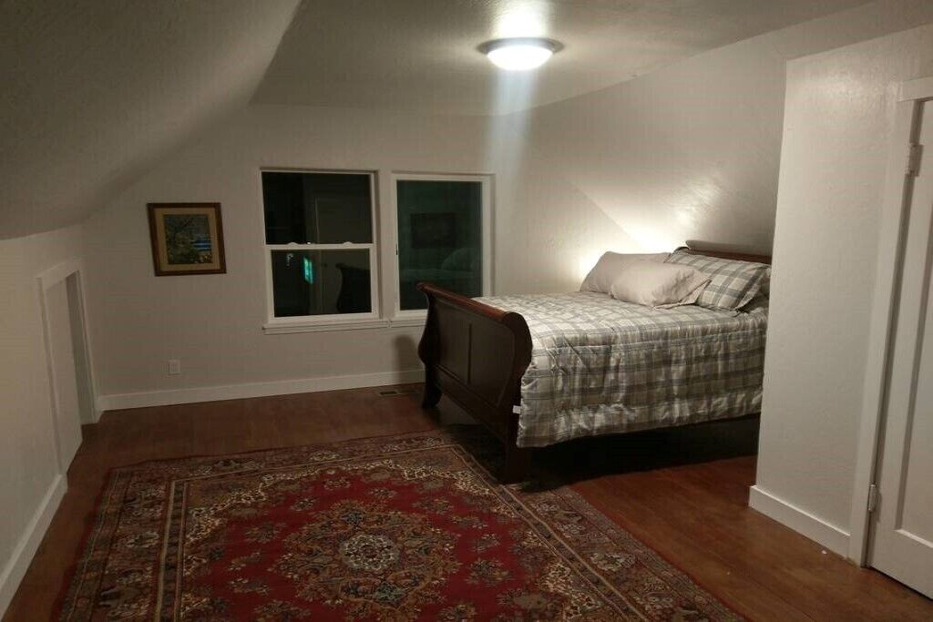 A bedroom with a bed, a window, a door, and a red patterned rug.