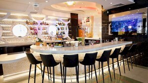 A modern bar area with a curved counter, black bar stools, and a large screen displaying a cityscape. - Cardozo Hotel South Beach (Miami Beach)
