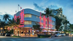A hotel with a curved facade, palm trees, and outdoor seating areas. - Cardozo Hotel South Beach (Miami Beach)