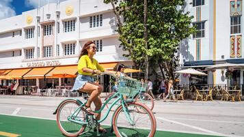 A woman riding a bicycle with a basket on a street with a green bike lane, in front of a building with a sign reading "CARDERO HOTEL".