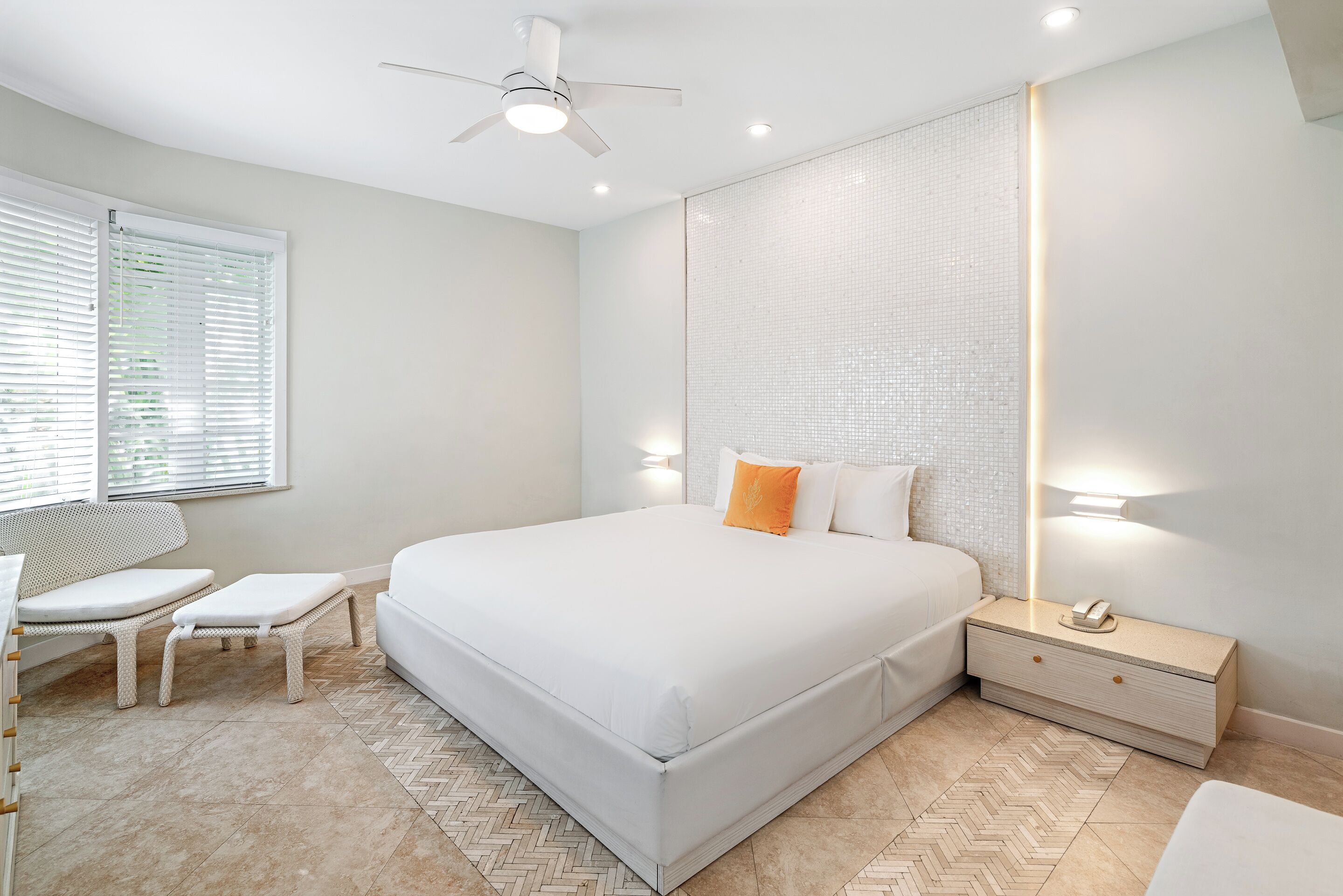 A modern bedroom with a large bed, bedside tables, a chair, and a ceiling fan.