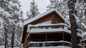 Une cabane en bois à plusieurs étages, dotée de balcons et entourée d’arbres couverts de neige.