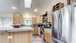 Une cuisine moderne avec des meubles en bois, des appareils en acier inoxydable et un grand îlot central agrémenté d’un panier de fruits.