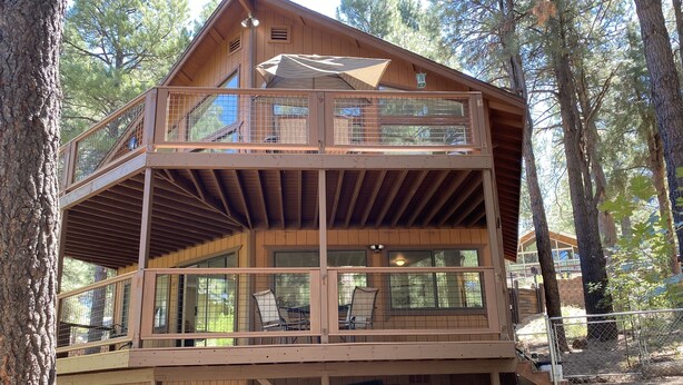 Une cabane en bois à plusieurs niveaux, dotée d’un balcon, de grandes fenêtres et d’un espace extérieur couvert.