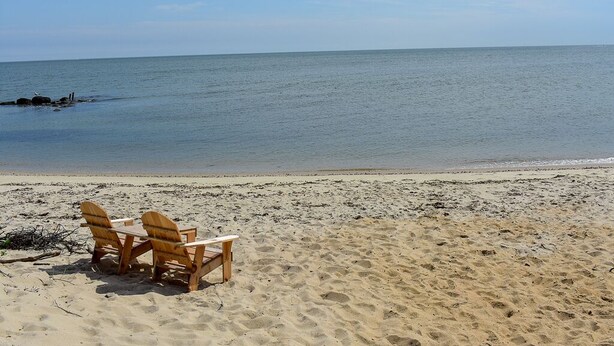 Ein Strand mit zwei Holz-Adirondack-Stühlen und einem Tisch.