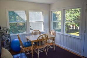 Enjoy a peaceful view of the lush outdoor area from the bay window in this serene room, featuring a dining table and comfortable seating for four.