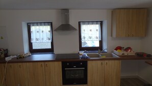 Una cocina con armarios de madera, horno empotrado, pileta y dos ventanas con cortinas.