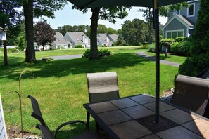 A patio with a table and chairs, surrounded by a lawn and trees.