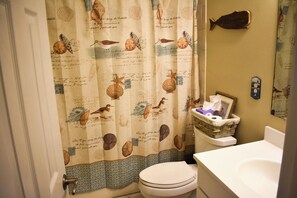 A bathroom with a toilet, a sink, and a shower curtain with a nautical theme.