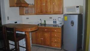 Een keuken met houten kastjes, een magnetron, een koelkast, een gootsteen en een eethoek met een tafel en stoelen.