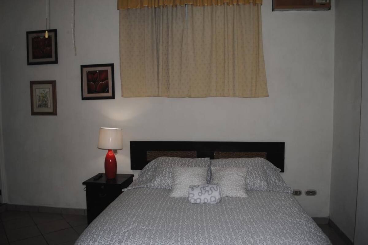 A bedroom with a bed, a nightstand, a lamp, and a window with curtains.