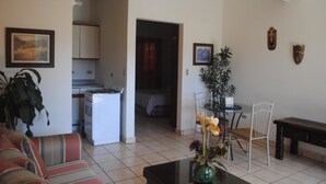 Een woonkamer met een bank, een eettafel met stoelen, een keukenhoek en een doorgang naar een slaapkamer.