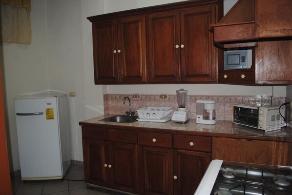 Una cocina con armarios de madera, un refrigerador, un lavamanos, un tostador, una licuadora y un microondas.