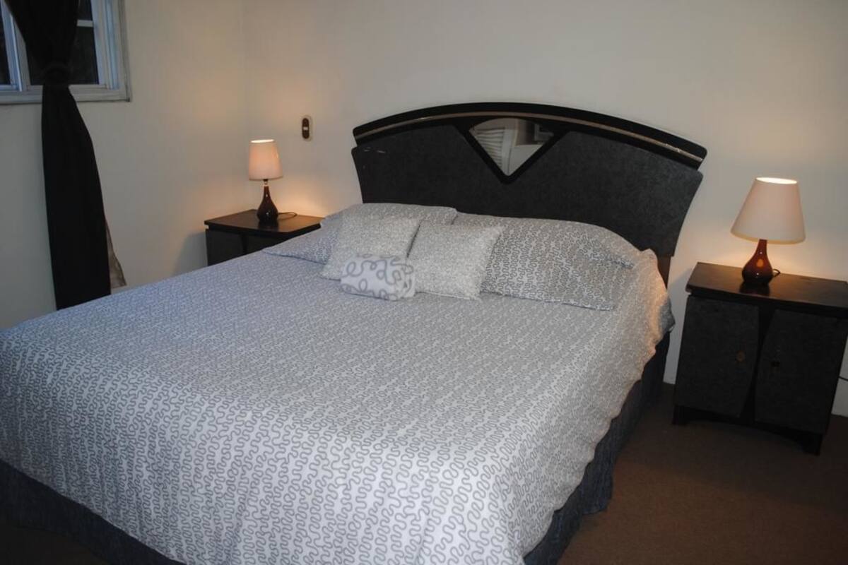 A neatly made bed with patterned bedding, two bedside tables with lamps, and a dark headboard.