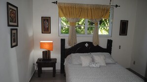 Een slaapkamer met een bed, nachtkastje met lamp, raam met gordijnen en ingelijste foto's aan de muur.