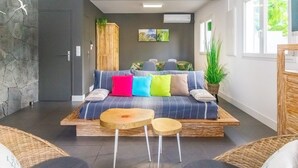 A modern living room with a sofa, two wooden tables, wicker chairs, a ceiling fan, and a stone wall. - Lagoon! Pretty villa at 2 steps from the lagoon of Saline les bains (La Saline-Les-Bains)