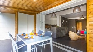 A modern dining area with a white table and chairs, a kitchen in the background, and a wooden ceiling. - Lagoon! Pretty villa at 2 steps from the lagoon of Saline les bains (La Saline-Les-Bains)