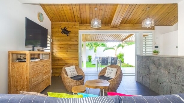 A cozy room with a wooden ceiling, a flat-screen TV, wicker chairs, a small round table, and a sofa with colorful cushions. - Lagoon! Pretty villa at 2 steps from the lagoon of Saline les bains (La Saline-Les-Bains)