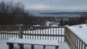 Une terrasse en bois avec un banc, donnant sur un paysage enneigé parsemé d’arbres et sur une étendue d’eau au loin.