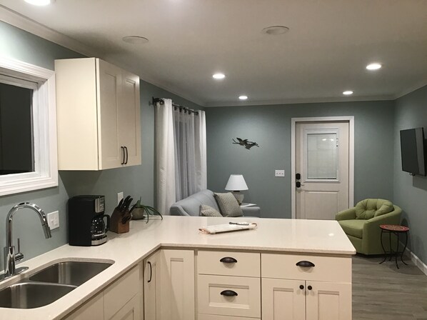 A compact kitchen with a sink, cabinets, a coffee maker, and a small table with a lamp.