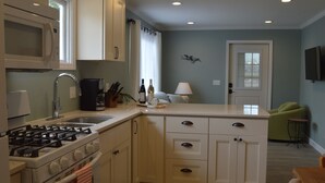 Une cuisine avec des meubles blancs, une cuisinière à gaz, un évier et une fenêtre avec un rideau.