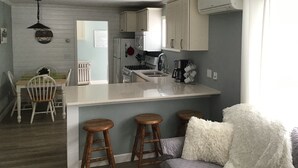 Une cuisine compacte dotée d’un îlot central, de tabourets en bois et d’un coin salon confortable agrémenté d’un coussin blanc moelleux.